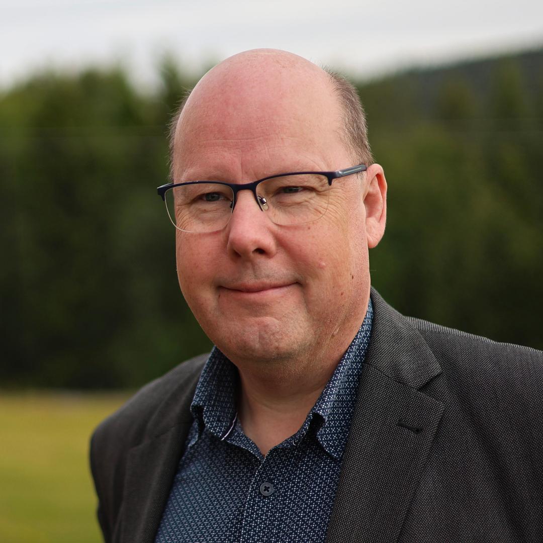 En man med glasögon, klädd i kavaj, tittar in i kameran.