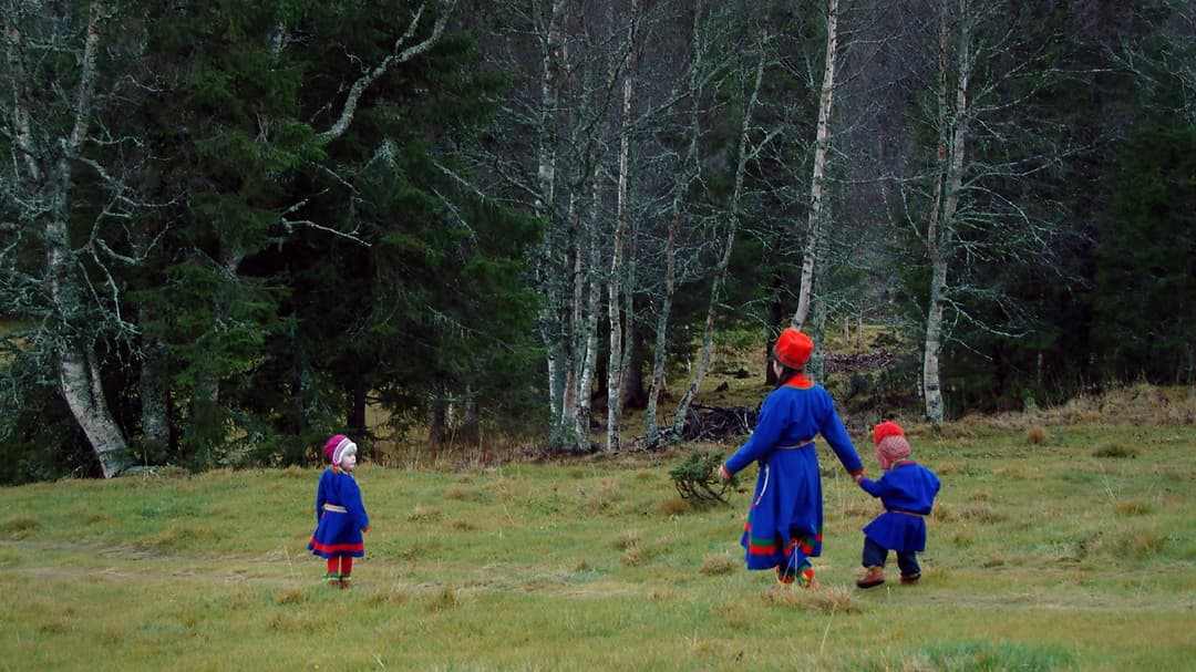 Kvinna och två barn i sydsamiska dräkter går över ett fält.