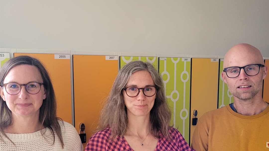 Två kvinnor och en man står framför gula skåp i en skola