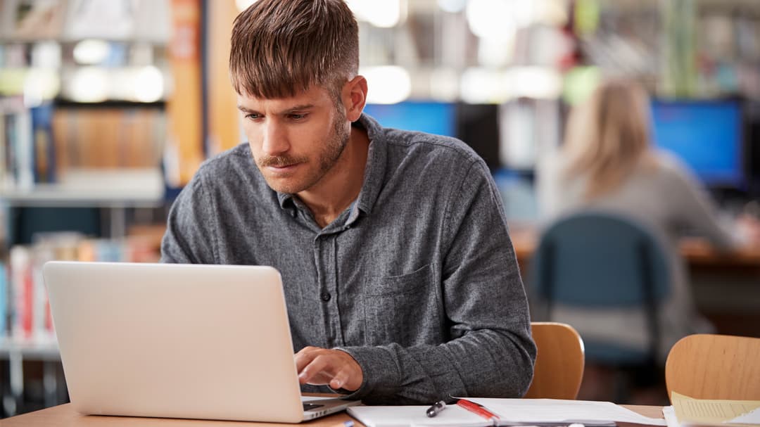 23592951-mature-male-student-working-on-laptop-in-college-library.jpg