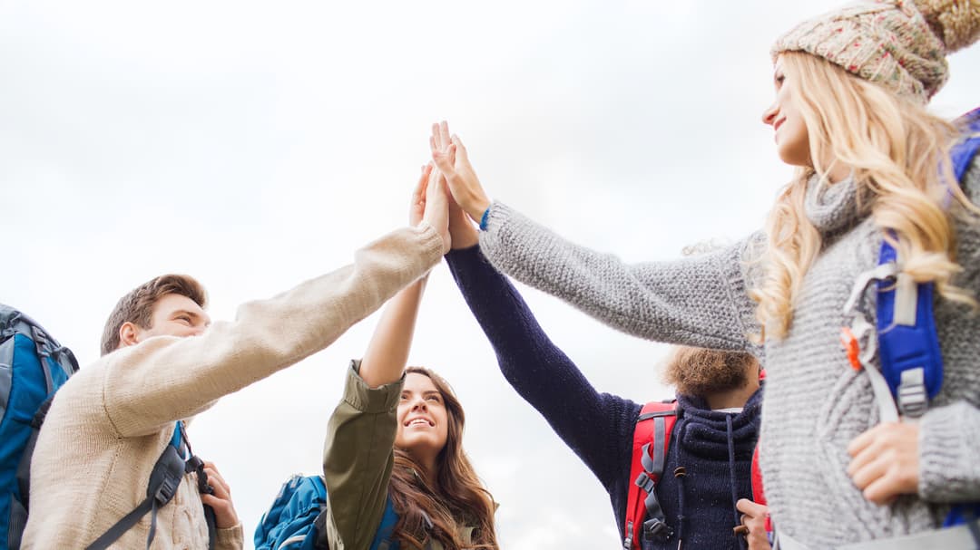 En grupp människor med ryggsäckar på sig står i en ring och gör en high five