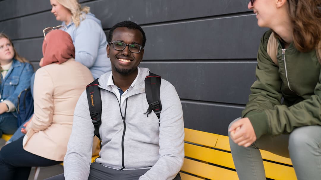 Två studenter som sitter på gul bänk och pratar med varandra. 
