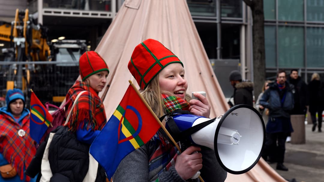 Woman holding a Saami flag and speaking in a megaphone.