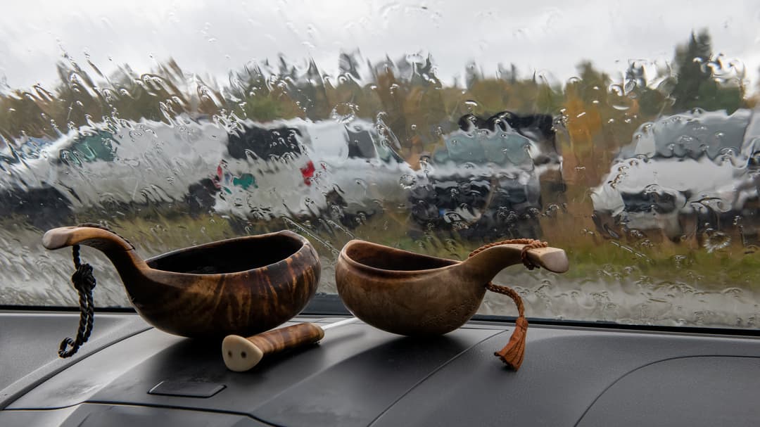 Två samiska kåsor och en samekniv i framrutan på en bil med intensivt regn utanför.
