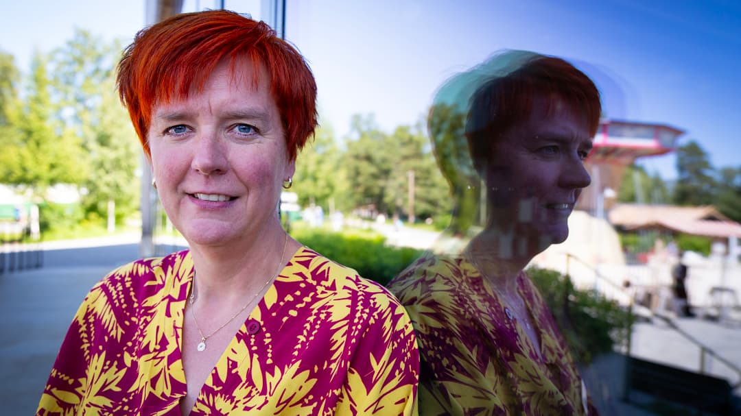 En kvinna sitter med ryggen mot ett fönster som återspeglar henne. 