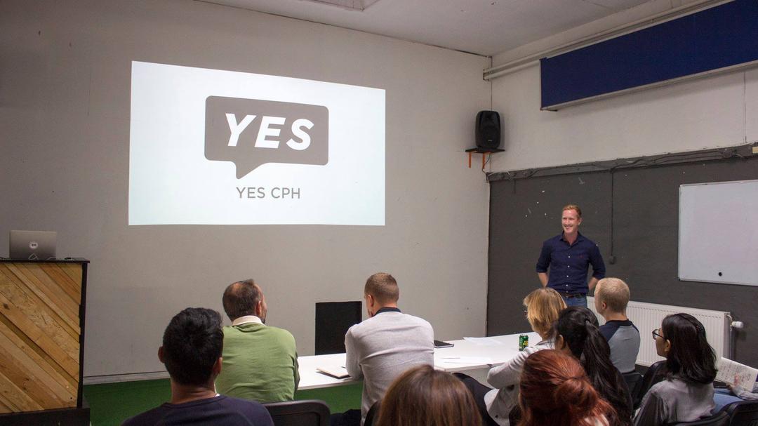 Grupp sitter vid bor i ett rum och tittar på en presentation