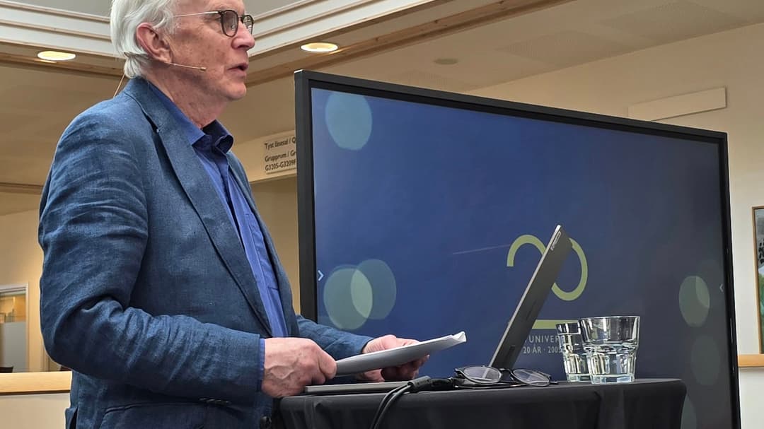 Gråhårig man i kavaj håller föredrag framför en bildskärm