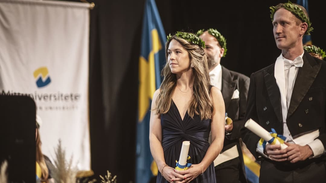 Finklädda personer med lagerkransar står på en scen med diplom i handen.