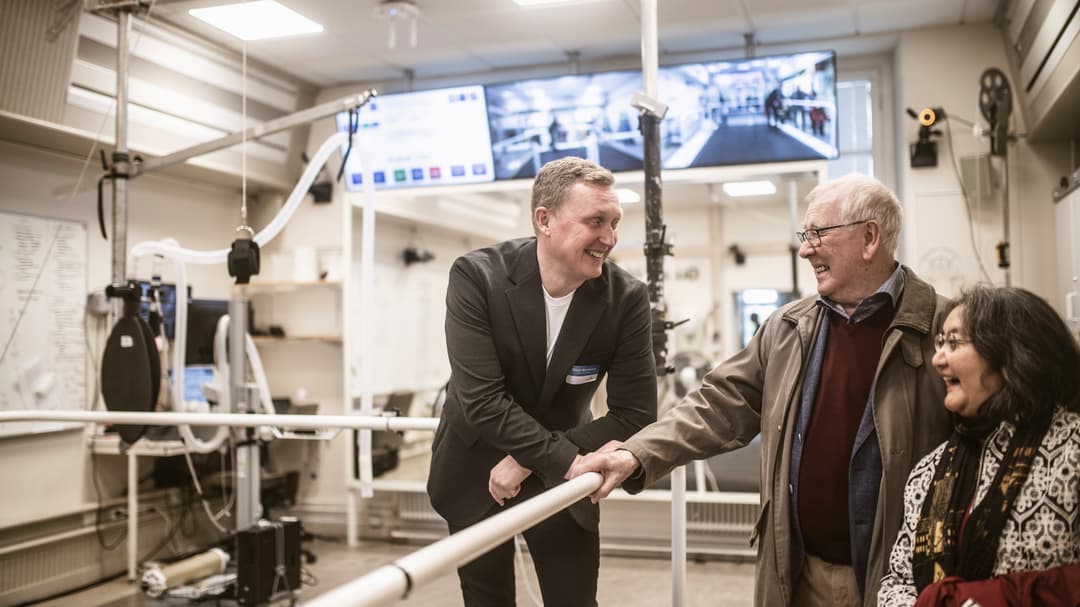 Man står lutandes mot staket och ler mot glad kvinna och glad man i ett forskningslabb. 
