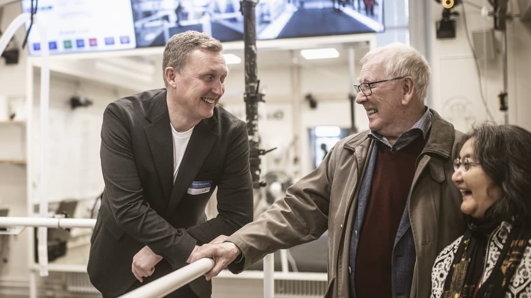 A man leans against a fence, smiling at a cheerful woman and a cheerful man in a research laboratory.
