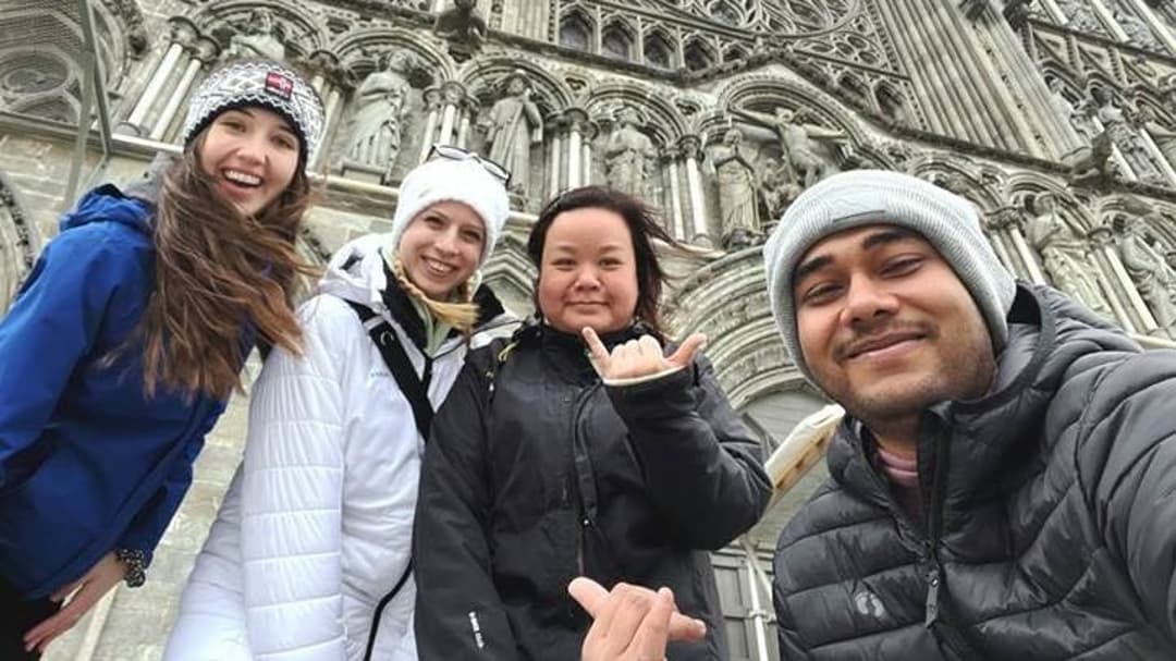 Fyra glada, unga människor står framför en kyrka iklädda ytterkläder. 