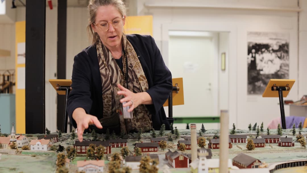 Kvinna står bredvid och visar en modell av en by i miniatyr 