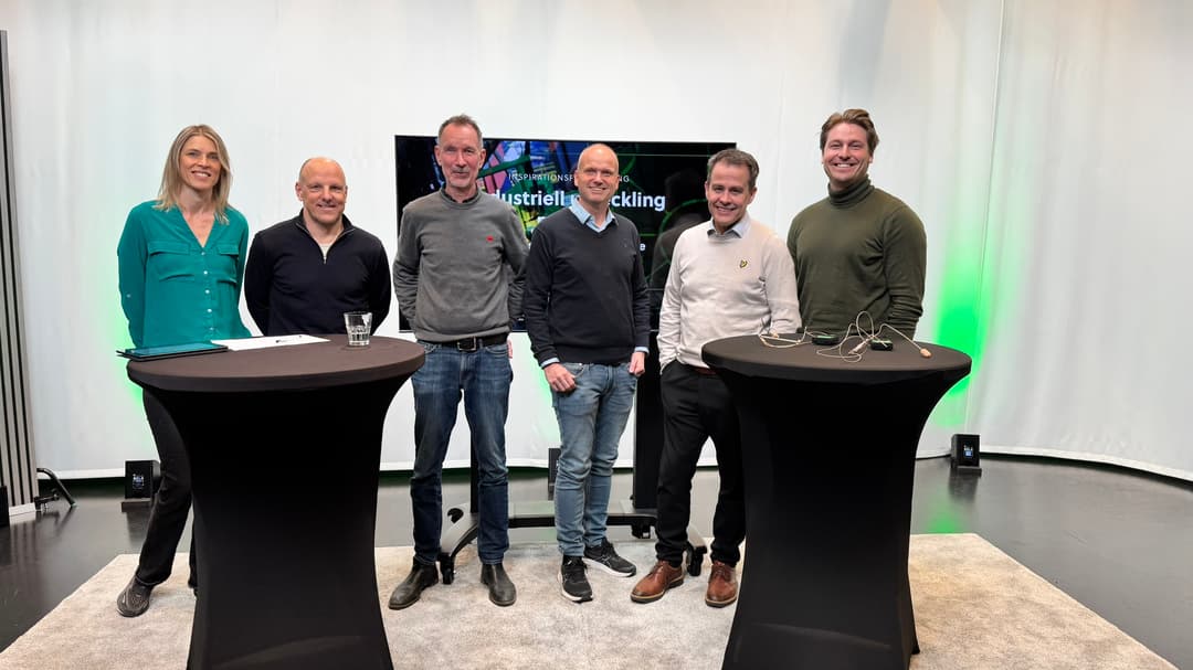 6 personer står bakom två stå bord och ler mot kameran