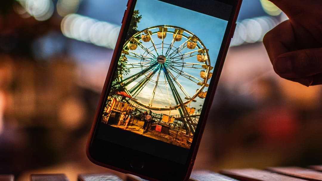 Metabild: Person tar en bild på ett Pariserhjul med mobilen och ser motivet både i mobilen och i verkligheten