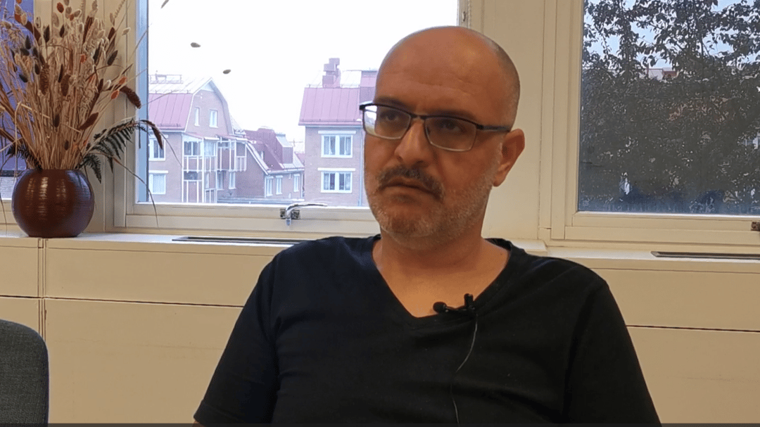 A man wearing glasses and a black shirt is being interviewed