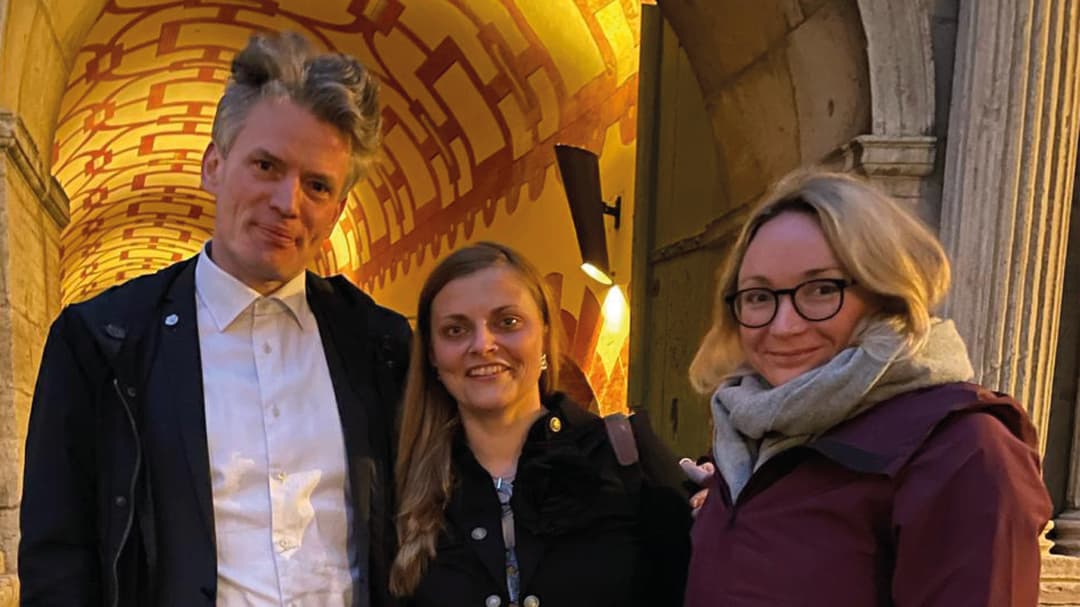Tre personer, en man och två kvinnor står framför ett upplyst stenvalv. 
