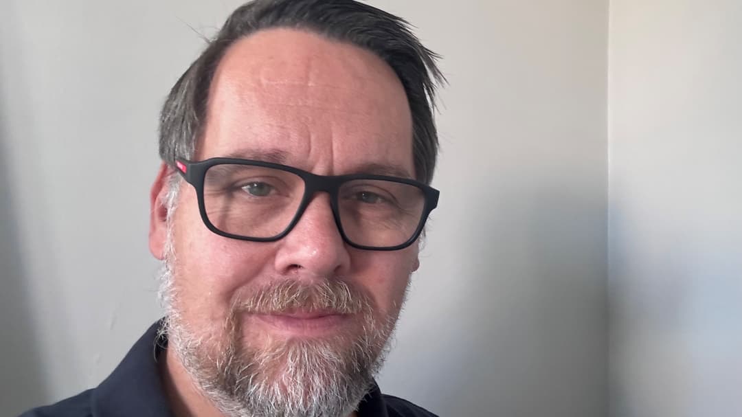 Porträttfoto av en man med brunt hår och mörka glasögon