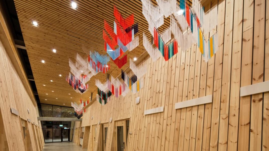 Konstverk av trådar i formen av samiska sidensjalar hänger från taket i träbyggnad av modern arkitektur.