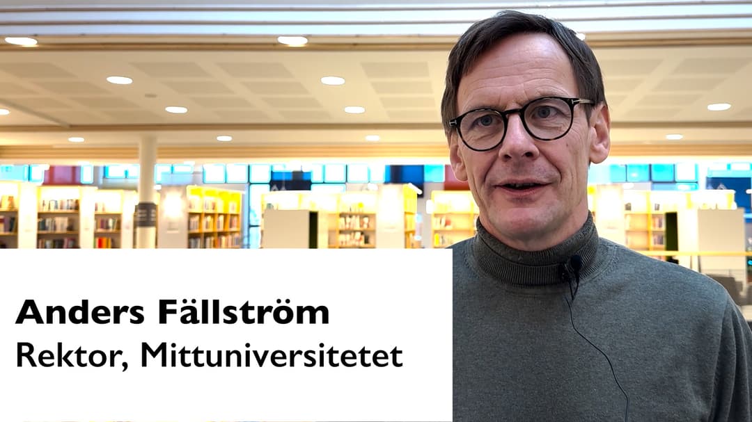 Man med glasögon, mörkt kortklippt hår, klädd i grå polo,  som står i ett bibliotek