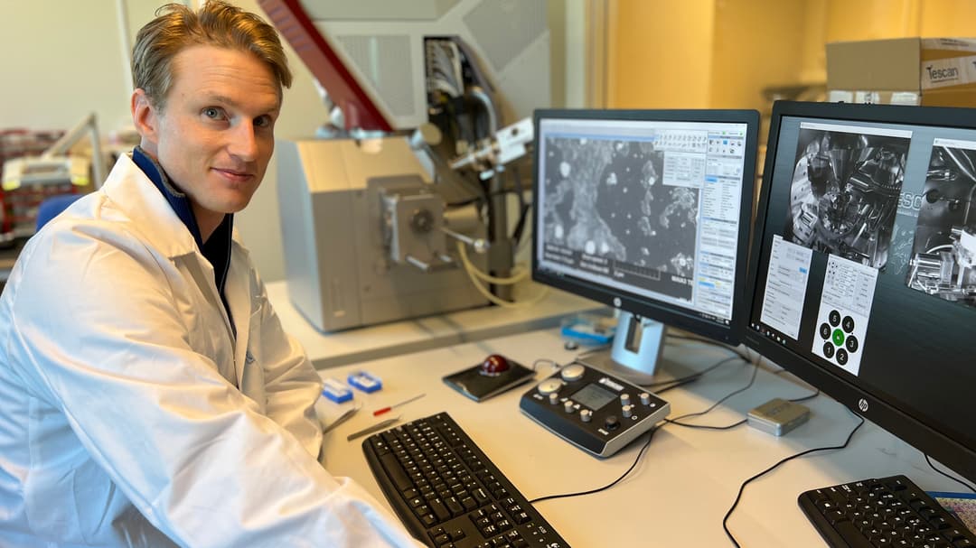 En man i vit labbrock sitter framför ett skrivbord med två bildskärmar.