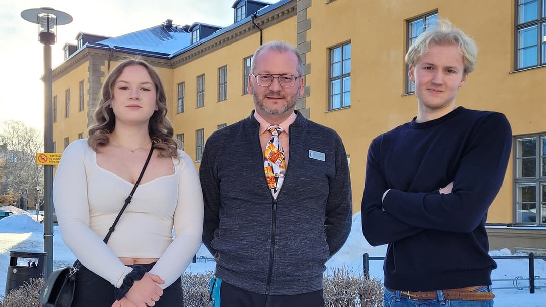 Tre personer står framför en gul byggnad med vita fönster på en snöig dag