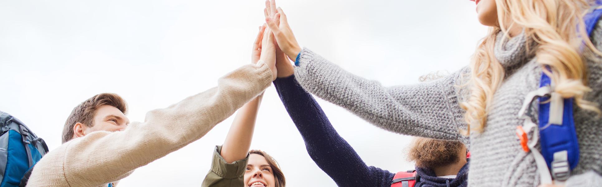 A group of people with backpacks on them stand in a ring and do a high five