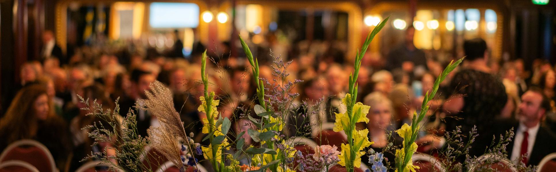 Blomsterarrangemang på en scen med uppradade stolar i bakgrunden.