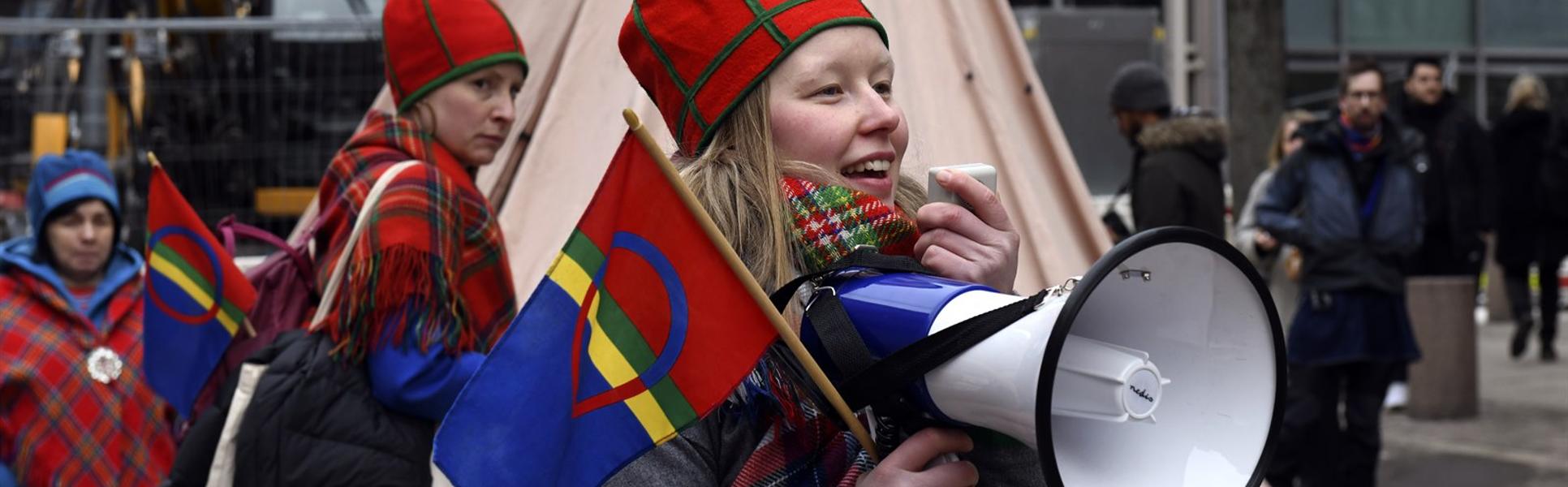 Kvinna håller en sameflagga och talar i en megafon.