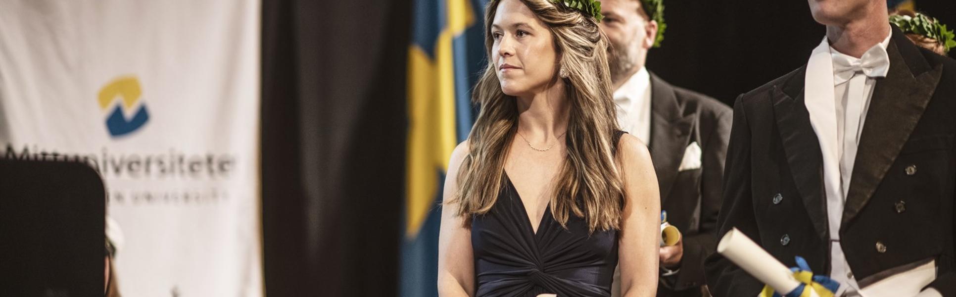 Finklädda personer med lagerkransar står på en scen med diplom i handen.