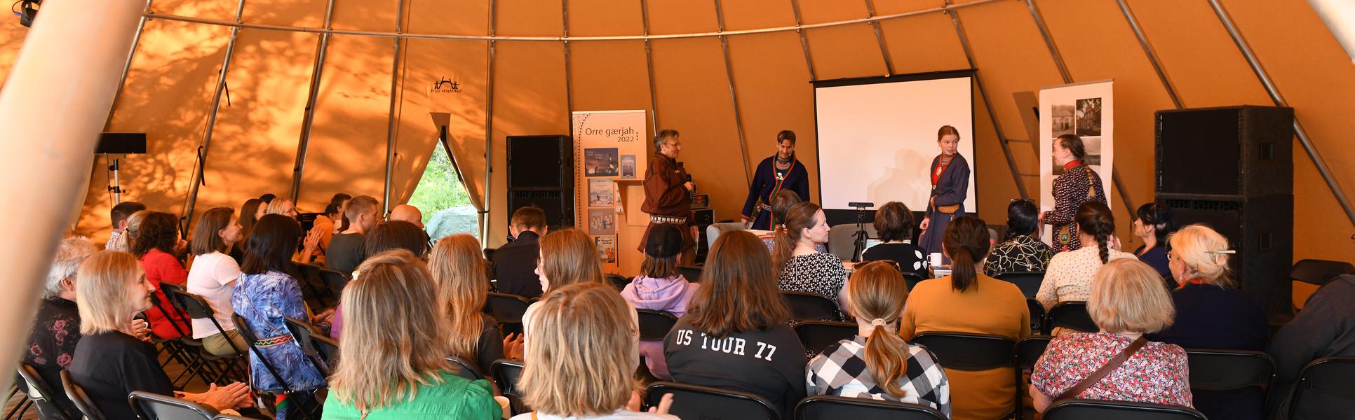 Publik lyssnar på ett panelsamtal i en stor tältkåta.