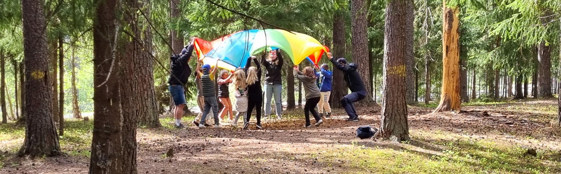 flera barn som håller upp ett färgglatt segel i skogen