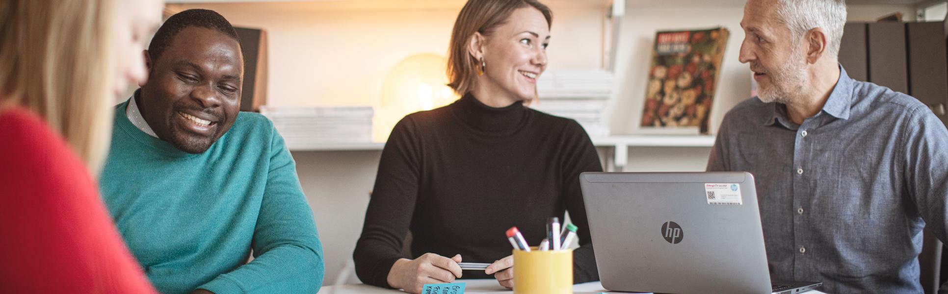 Fyra studenter runt ett bord som arbetar med en laptop och post-it lappar.