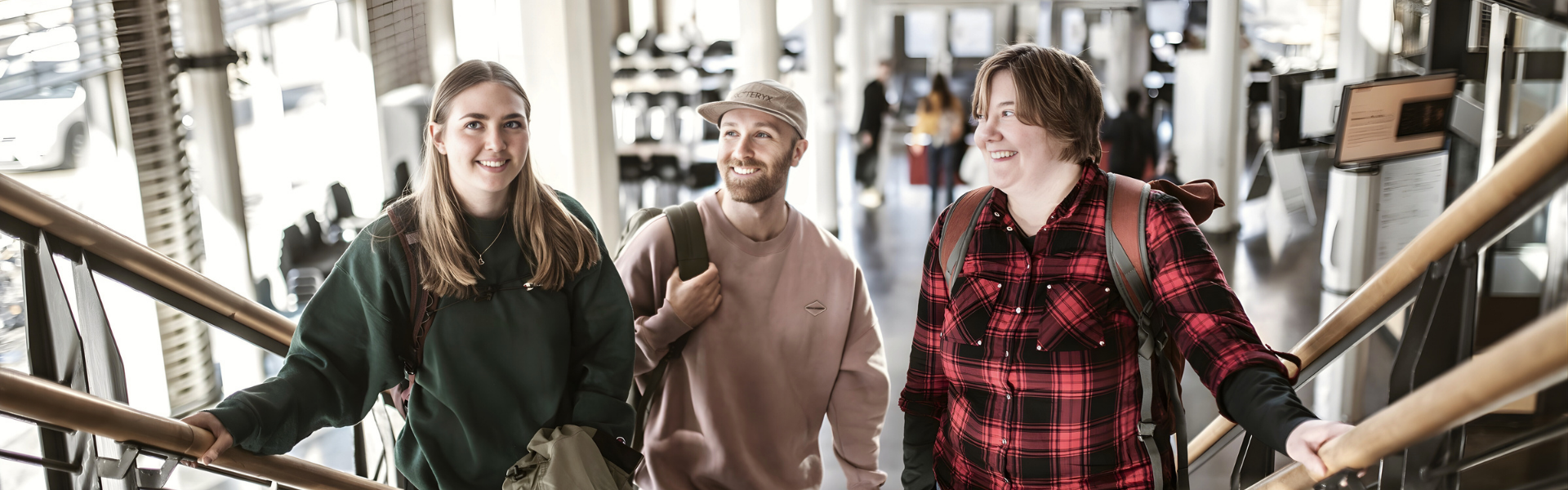 Tre unga studenter står i en trappa. De är alla glada. 