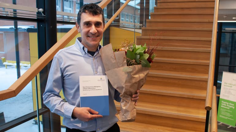 A happy man in posing infront of camera with a bouquet of flowers and his doctoral thesis.