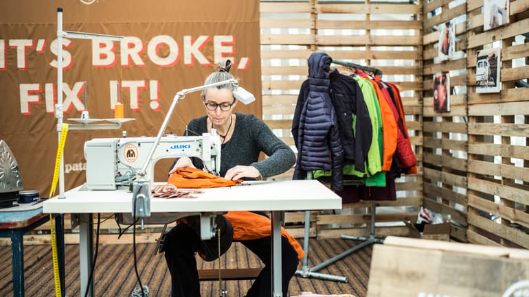 Kvinna sitter vid skrivbord och syr/lagar begagnade kläder på symaskin