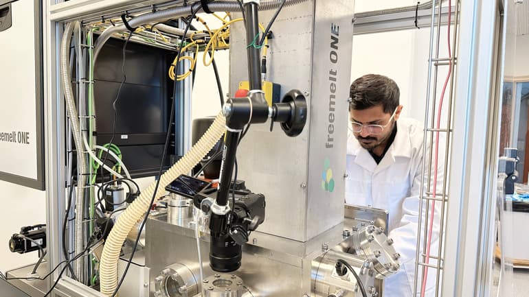 A man in a white coat working with a machine in a lab environment