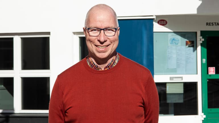 En man i glasögon och röd tröja med flera fönster i bakgrunden 