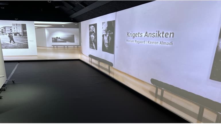 Exhibition space with projected photos and the text “Krigets Ansikten” with two names.