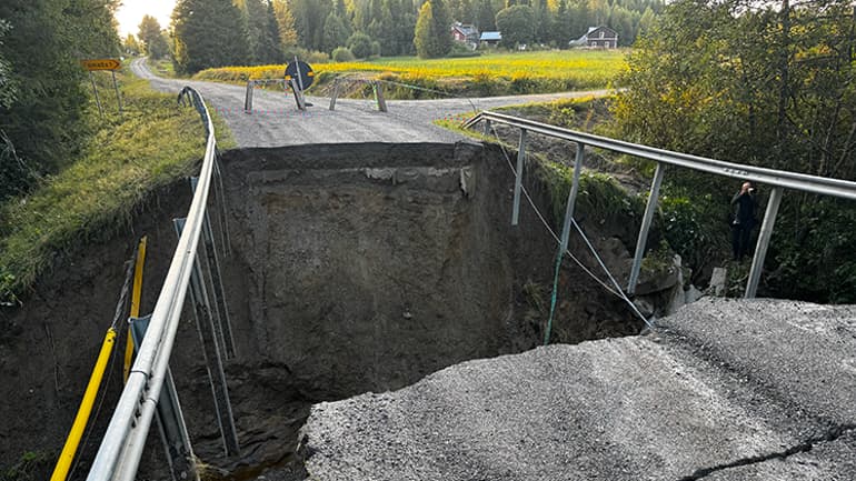 Rasat vägavsnitt med stort hål där bron har kollapsat, räcken hänger över kanten.