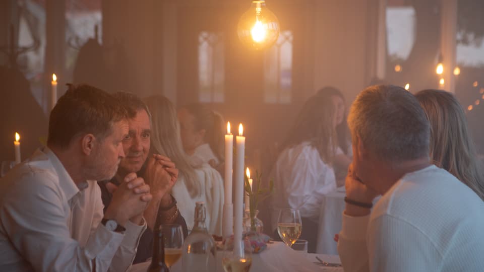 Människor runt matbord med levande ljus.
