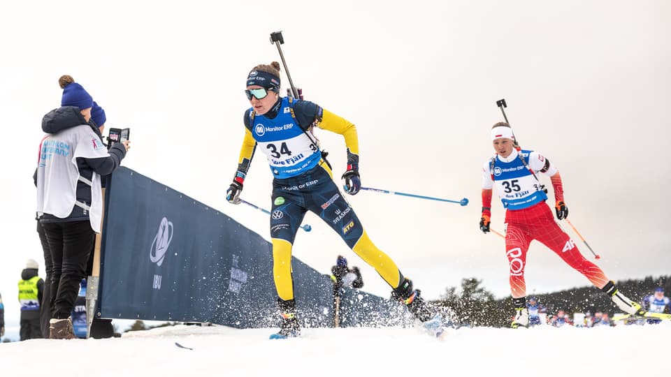 Skidskytt i svensk landslagsdress skidar mot kameran