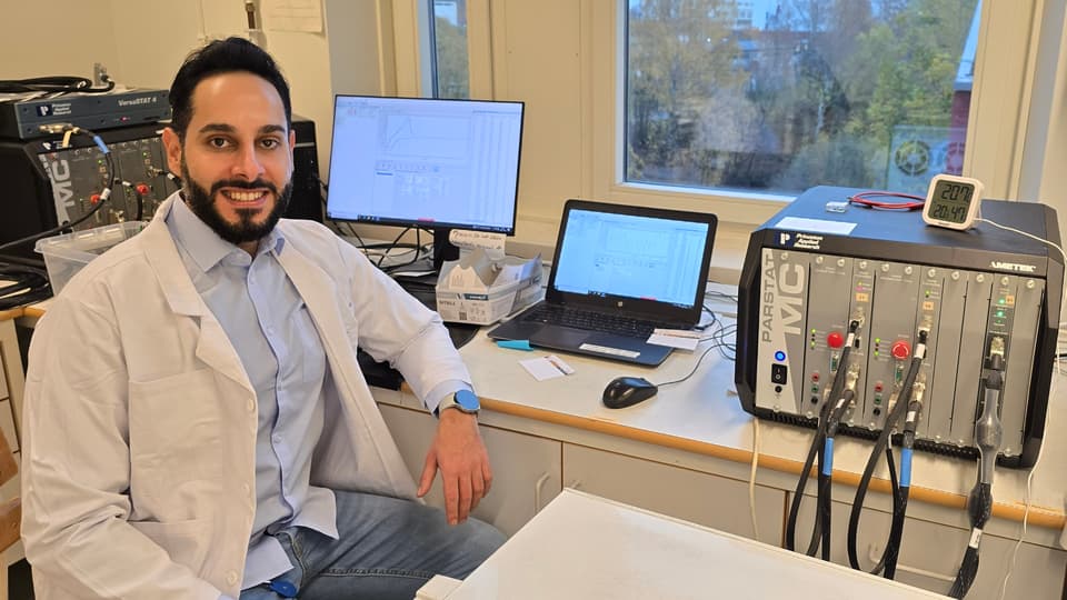 En man i en vit laboratorierock sitter vid datorer och laboratorieutrustning. 