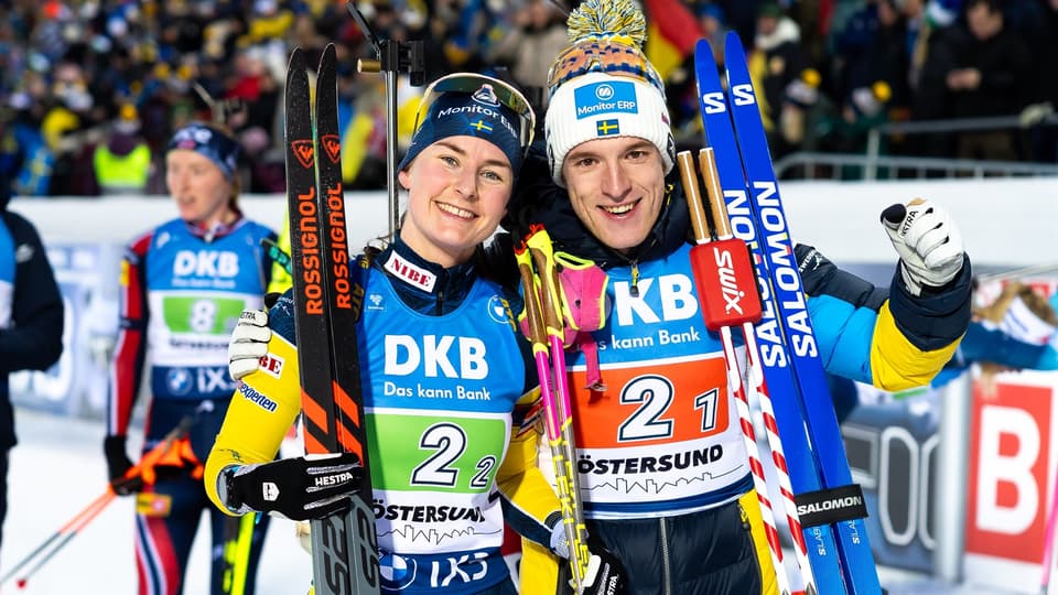 Två skidåkare bredvid varandra med tävlingskläder och skidor lutade mot axeln.