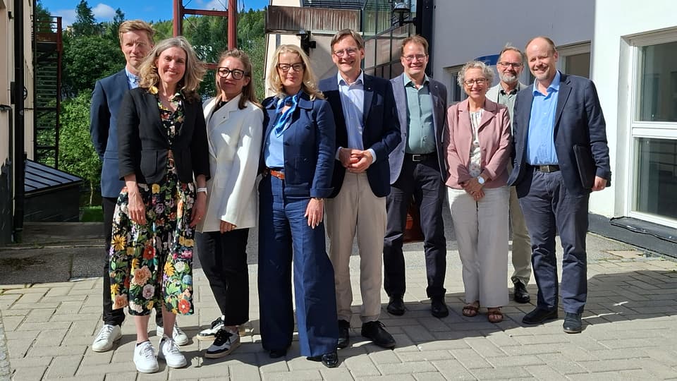 Gruppbild med nio personer ståendes utomhus i solen.