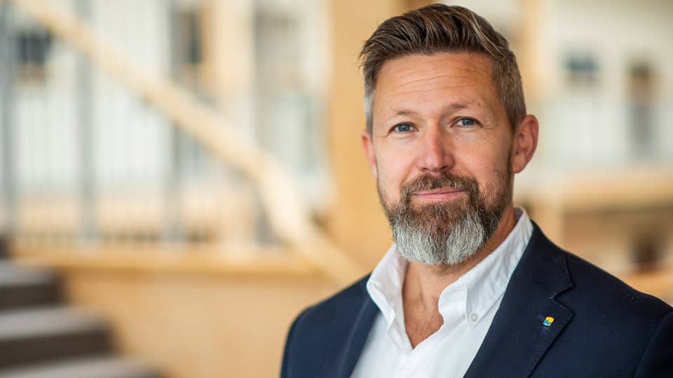 En man med skägg som har en vit skjorta och marinblå kavaj