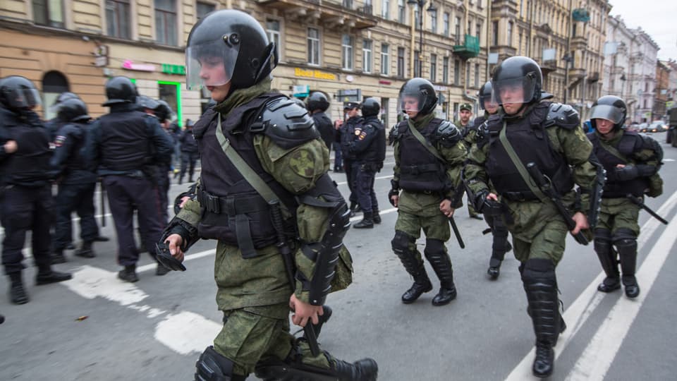 Armed soldiers in vests and helmets walk along a city street.