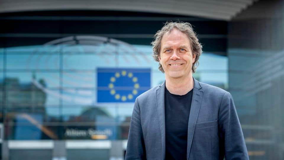 Leende man i kavaj framför glasbyggnad med EU-flagga