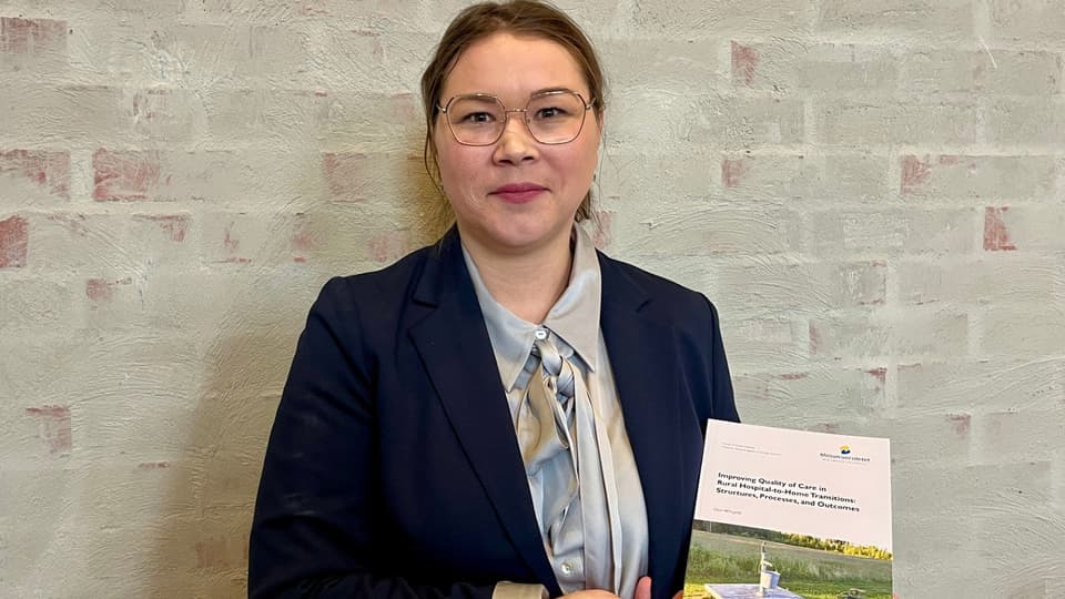 En mörkhårig kvinna med glasögon och mörkblå kavaj håller upp en bok.