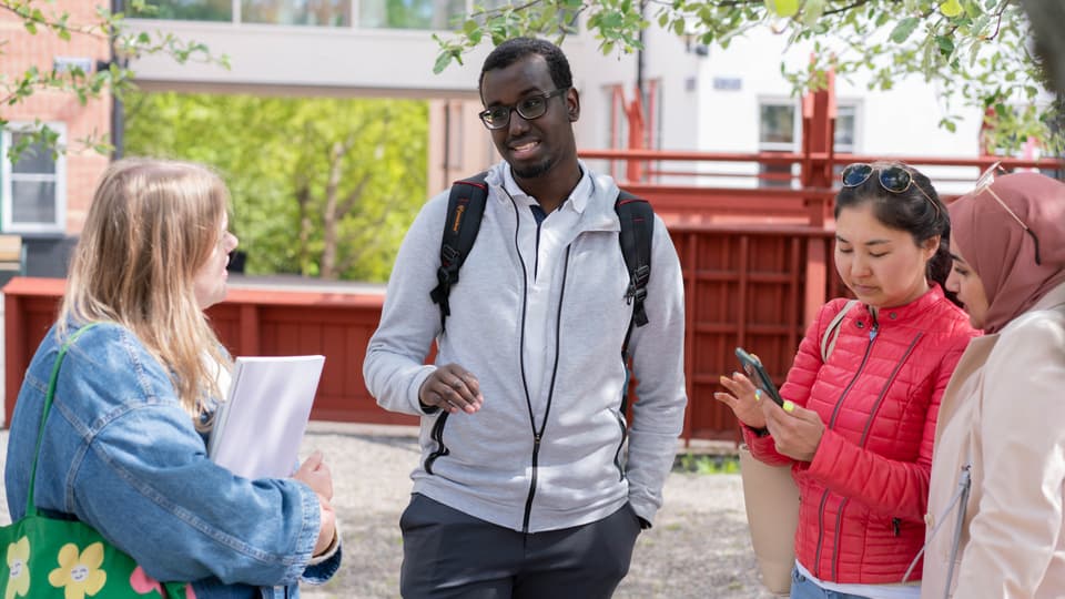 En grupp studenter som står och pratar med varandra utanför campus. 