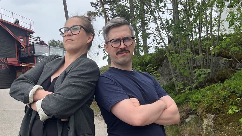 En kvinna och en man står bredvid varandra med lite träd och en byggnad i bakgrunden. 